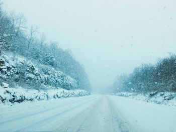 Snow covered road amidst trees during winter