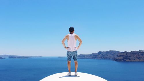 Rear view of man standing on boat in sea against clear blue sky