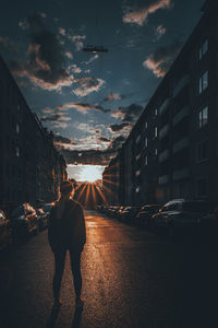 People walking on street amidst buildings against sky during sunset