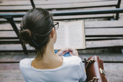 Rear view of woman reading book while sitting on bench