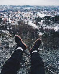 Low section of man sitting on mountain against sky during winter
