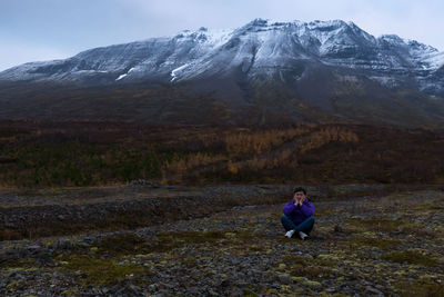 Man sitting on field against mountains