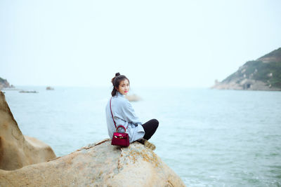 Portrait of woman sitting on rock by sea against clear sky