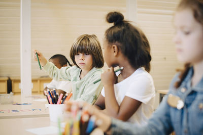 School friends drawing on paper at desk in classroom