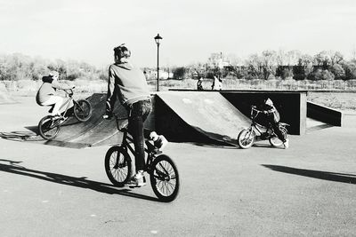Boys riding bmx bicycles at skateboard park against clear sky