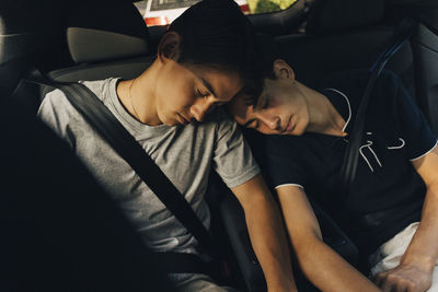 High angle view of teenage boy sleeping on brother's shoulder while sitting in car during road trip