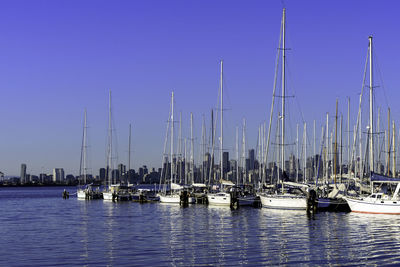 Sailboats moored in sea against clear blue sky