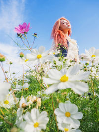 Low angle view of young woman with flowers blooming on field
