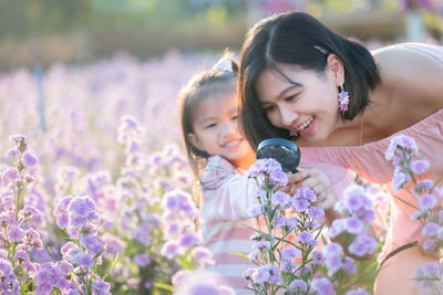 Cute girl looking through magnifying glass on flowering field with mother