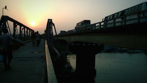 Bridge over river in city against sky during sunset