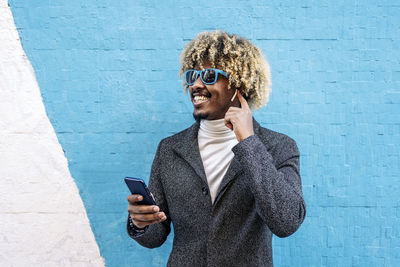 Young man using mobile phone while standing against wall