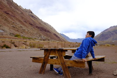 Man sitting on table by mountains against sky