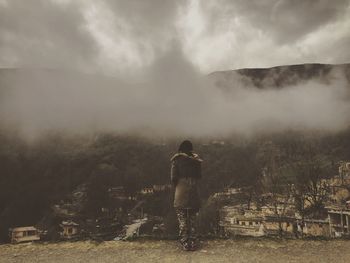 Woman standing on landscape against cloudy sky
