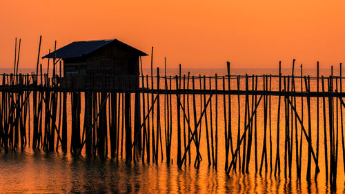 Silhouette wooden posts on house by building against orange sky