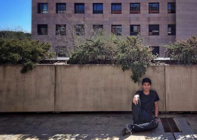 Portrait of man leaning on retaining wall while sitting outdoors