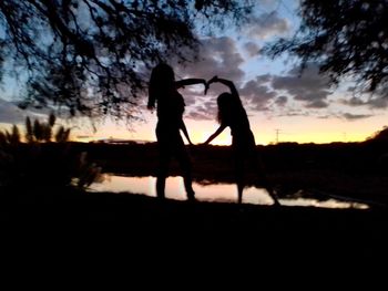 Silhouette couple standing on field against sky during sunset