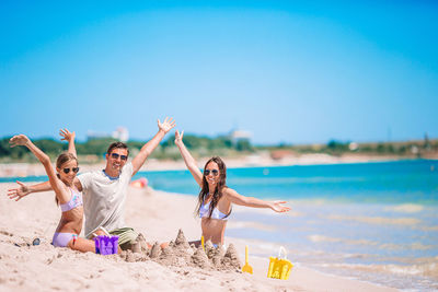 Full length of cheerful family with arms raised sitting on beach