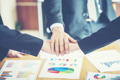 Business coworkers stacking hands over graphs at desk in office