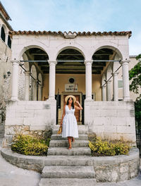 Young woman in white dress posing in front of old building, monument, architecture.