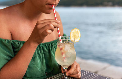 Close-up photo of woman drinking refreshing lemonade on straw in a bar by sea