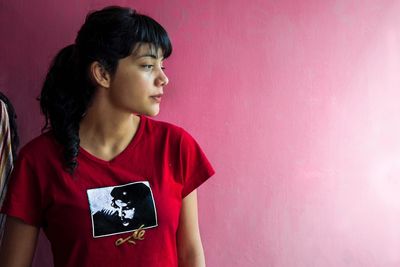 Woman looking away while standing against pink wall