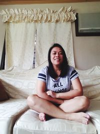 Portrait of smiling young woman sitting on sofa at home