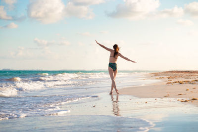 Rear view of woman wearing bikini while walking at beach against sky