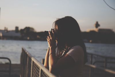 Woman photographing against sky during sunset