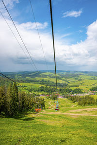 Empty ski lifts over beautiful green grassy covered hill against cloudy sky