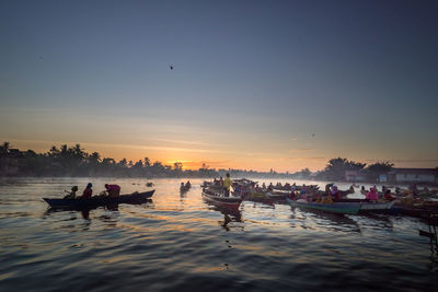 People in boats on river against sky during sunset