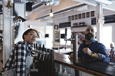 Female bartender with male customer looking up while standing at bar counter