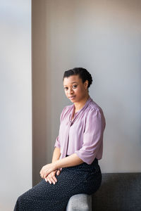 Portrait of confident businesswoman sitting on sofa against wall at office