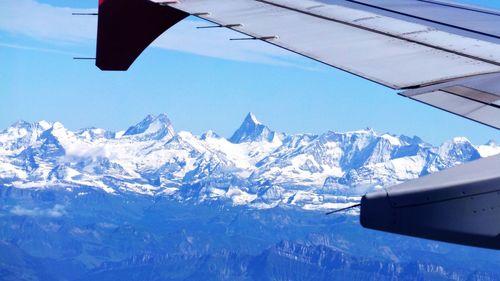Cropped image of airplane over snowcapped mountain against sky