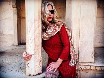 Mature woman wearing sunglasses and traditional clothing sitting against old building