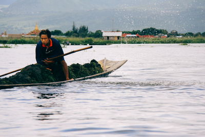 Man sailing boat in lake against sky