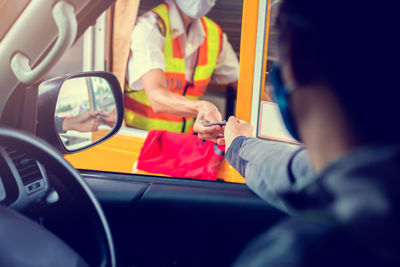 Rear view of man paying at tollbooth from car