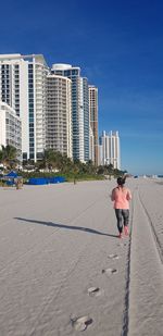 Rear view of woman running on sand at beach in city