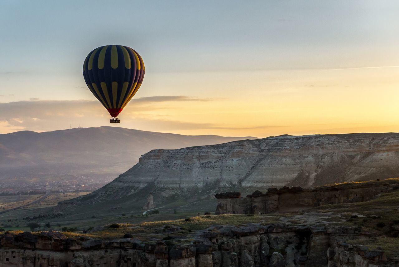 hot air balloon, rock formation, mountain, rock - object, mid-air, flying, sky, nature, beauty in nature, scenics, sunset, transportation, ballooning festival, adventure, no people, rock hoodoo, outdoors, landscape, day