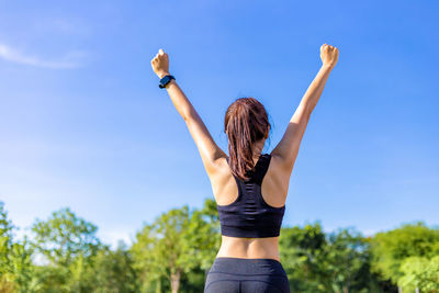 Rear view of woman with arms raised against sky