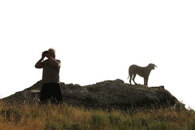 Man photographing with dog on rock against sky
