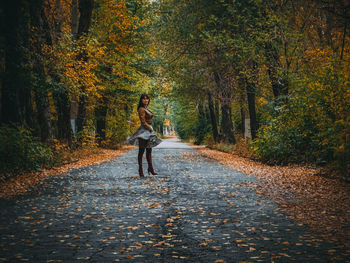 Full length of woman standing on road amidst trees during autumn