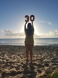 Rear view of young woman standing with number balloons at beach