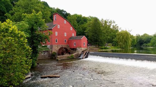 House by river amidst trees and building against sky