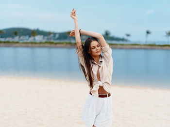 Full length of young woman with arms outstretched standing at beach