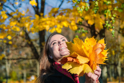 A woman with long hair rejoices at a yellow bouquet of leaves in an autumn park. autumn season.