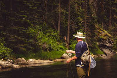 Rear view of man wearing hat fishing in river