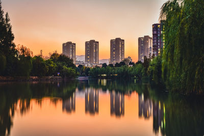 Reflection of trees and buildings in lake during sunset