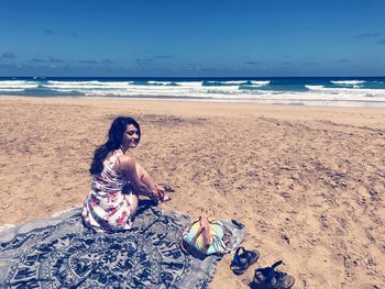 Woman sitting on beach by sea against sky