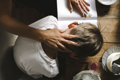 Mother's hand caressing tired son while studying at home