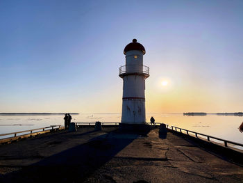 Lighthouse by sea against sky during sunset